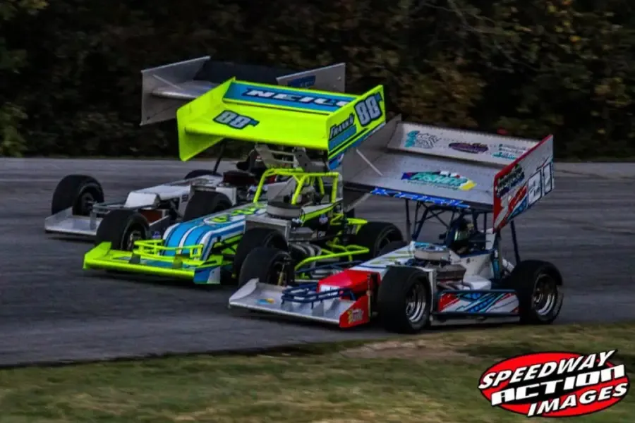 Supermodifieds racing side by side at dusk