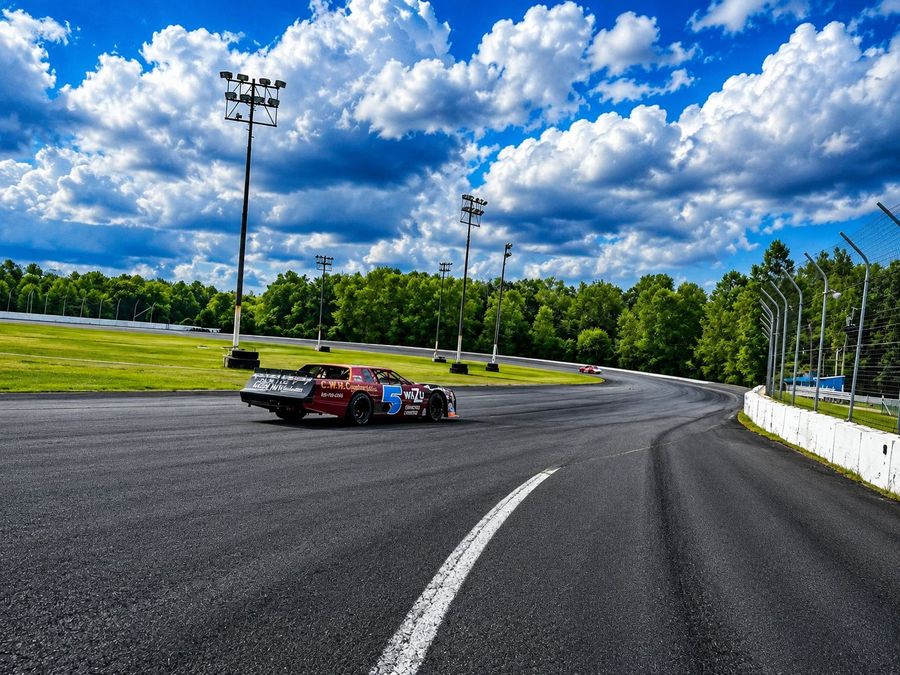 A street stock heading into turn one on a sunny day